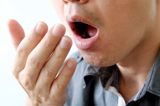 causes-of-bad-breath (3) man checking breath for causes of bad breath